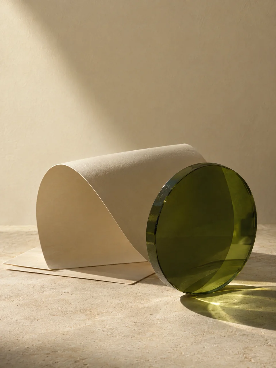 An olive-green glass lens casting clear sunlight across sculptural ivory paper.